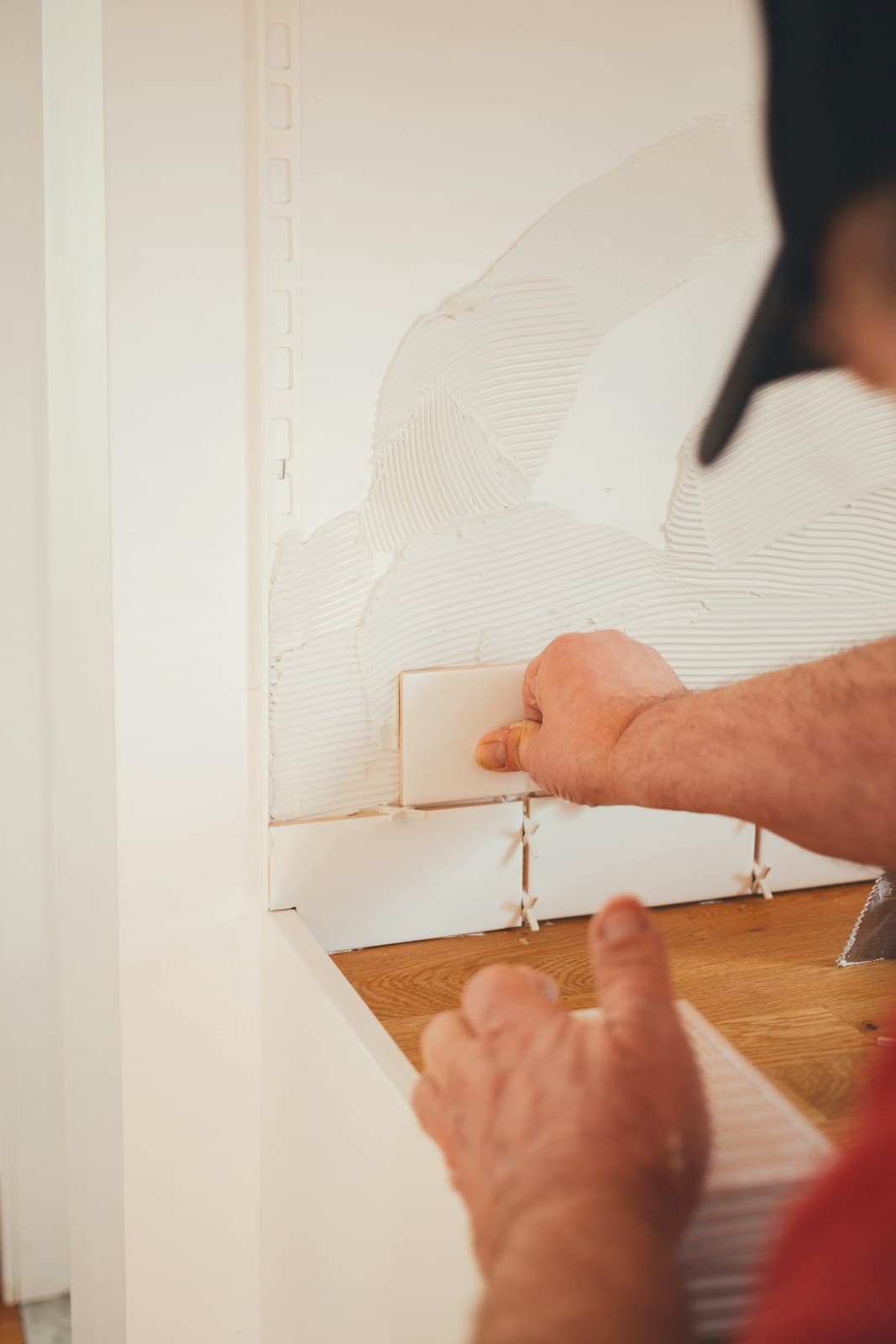 Hands pressing a white tile onto combed adhesive, with spacers below