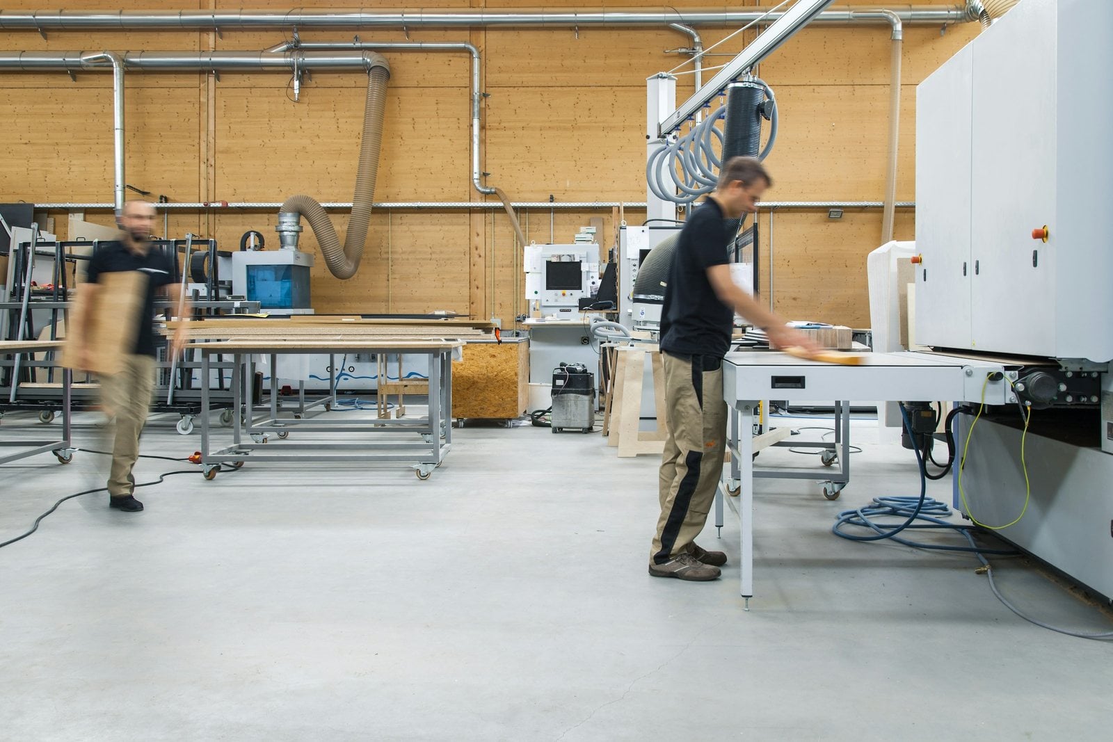 Two cabinet makers at work in a bright joinery workshop with panel machines