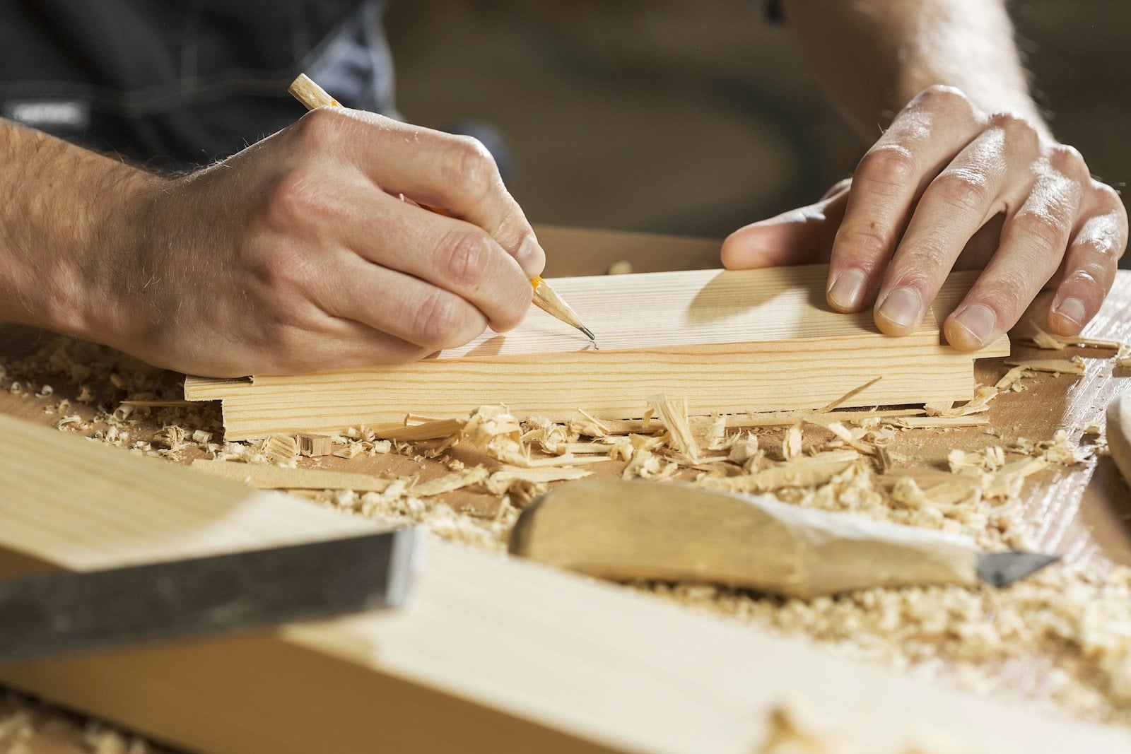 A carpenter’s hands marking timber with a pencil, among wood shavings