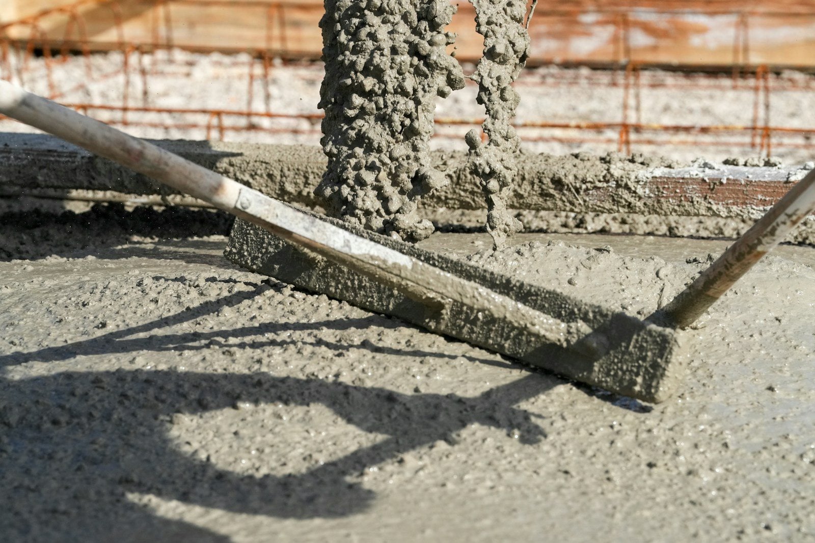Wet concrete pouring onto a slab while a long screed board levels it