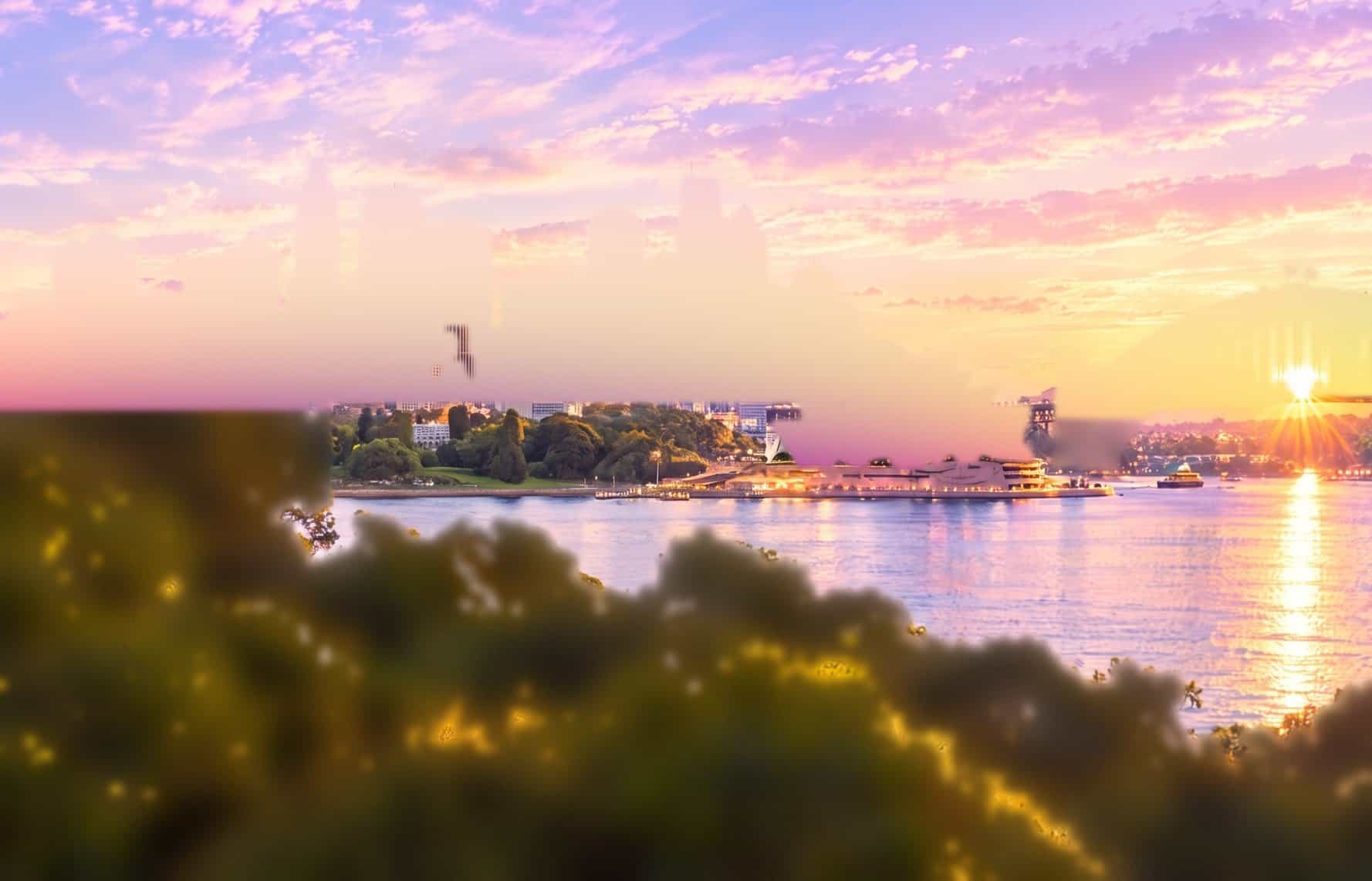 A tradesman in a hi-vis vest holding a tablet and looking up, with Sydney Harbour, the Opera House and the Harbour Bridge behind him at sunset
