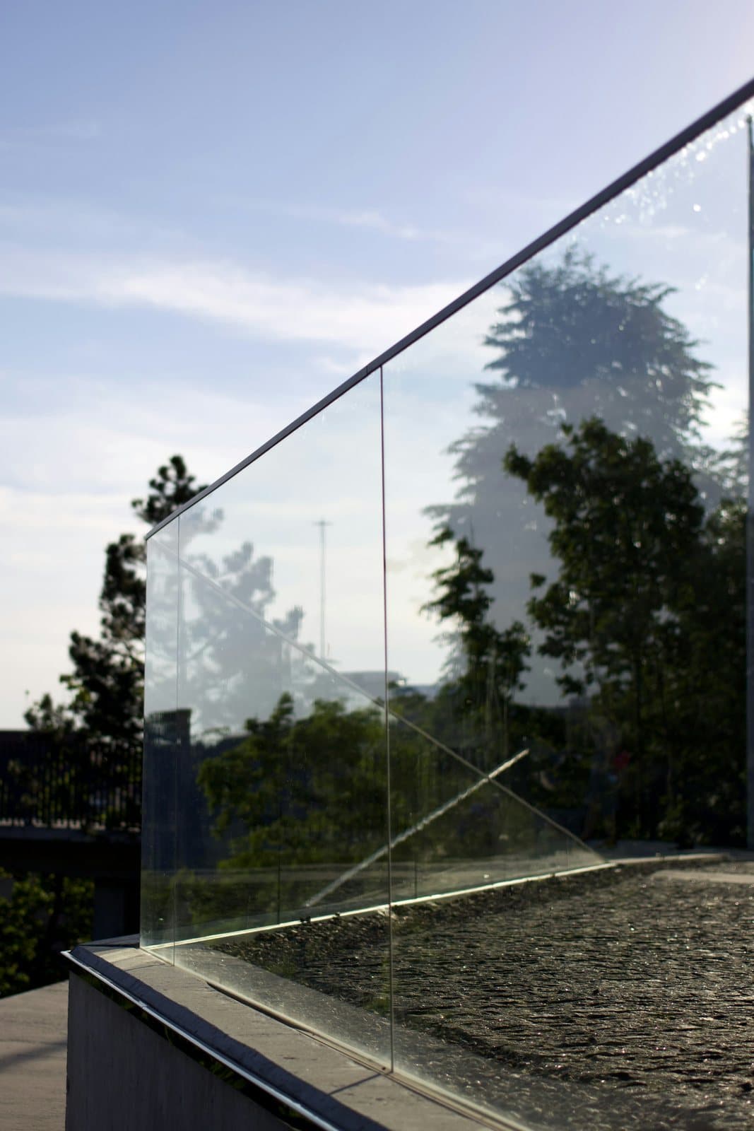 A frameless glass balustrade along a rooftop edge, with trees and sky behind