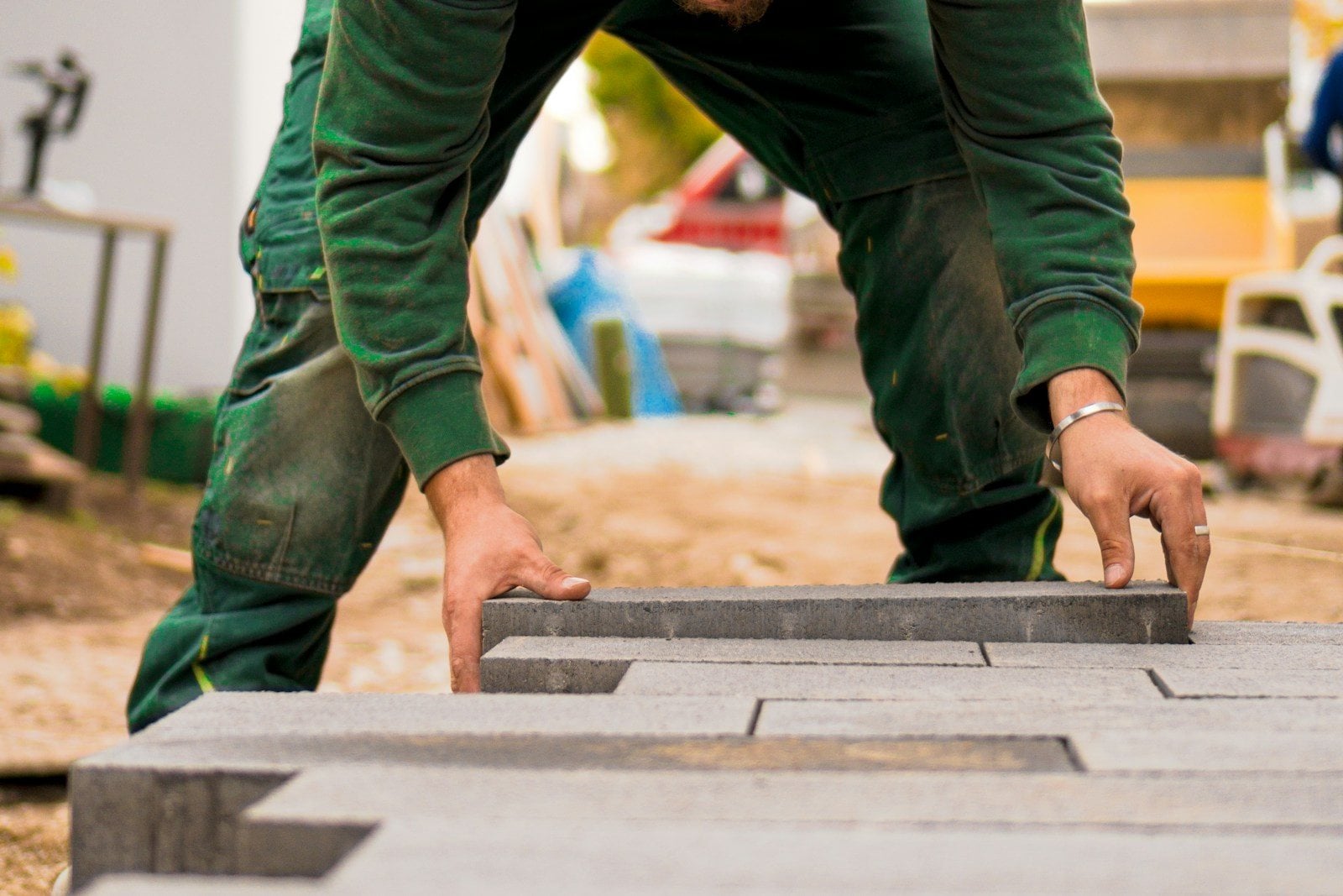 A landscaper in green work clothes setting grey concrete pavers