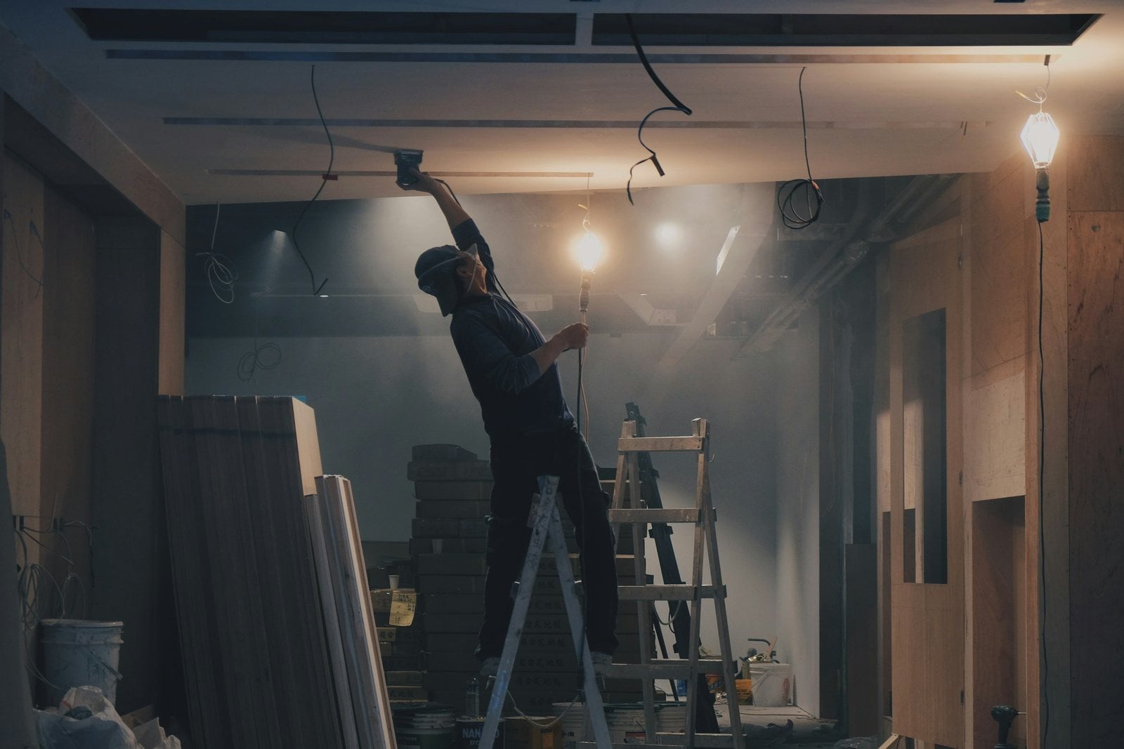 A tradesman on a stepladder working on a ceiling under bare work lights